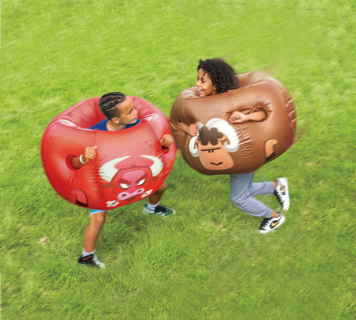 Two people wearing Rovers blow-up bumper balls featuring cartoon bull and sheep designs playing on green grass outdoors