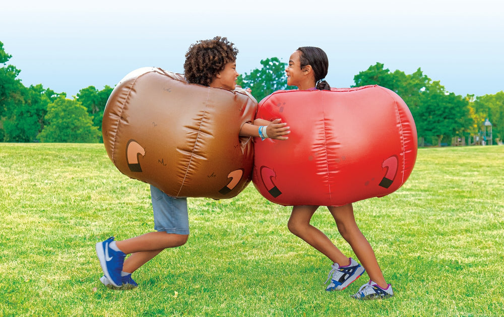 Two children playing outdoors wearing brown and red Rovers blow-up bumper balls on green grass